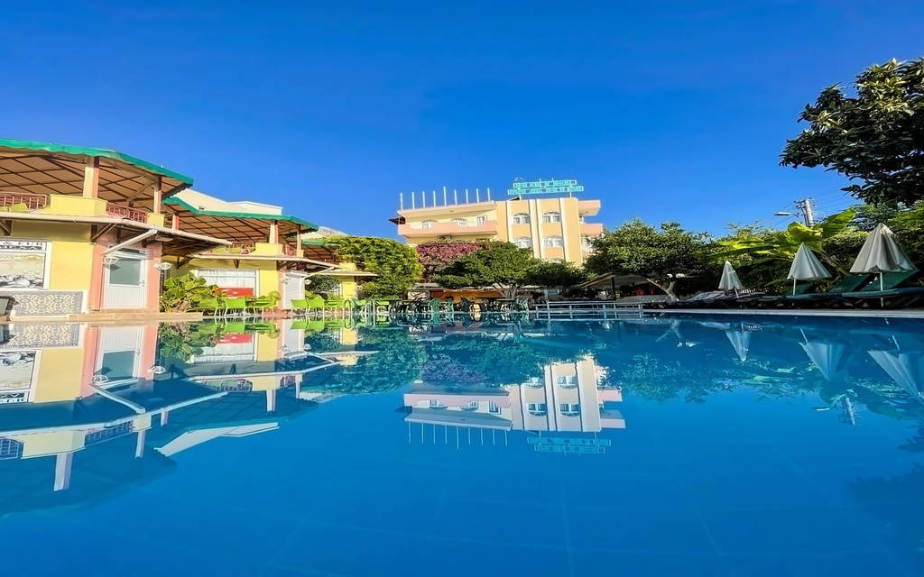 Jasně modrý bazén odrážející hotel a stromy pod jasně modrou oblohou. - Jasně modrý bazén odrážející hotel a stromy pod jasně modrou oblohou.