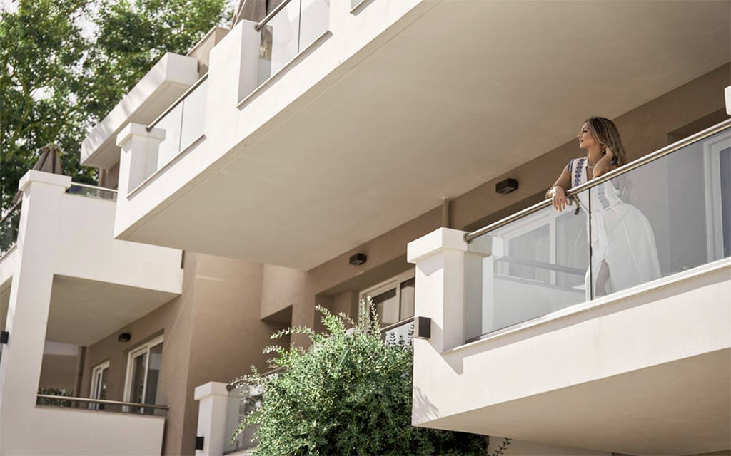 Žena v bílých šatech se opírá o zábradlí hotelového balkonu. - Žena v bílých šatech se opírá o zábradlí hotelového balkonu.