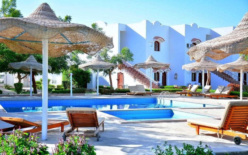 Oblast bazénu se slunečníky a lehátky, obklopená bílými budovami. - Oblast bazénu se slunečníky a lehátky, obklopená bílými budovami.