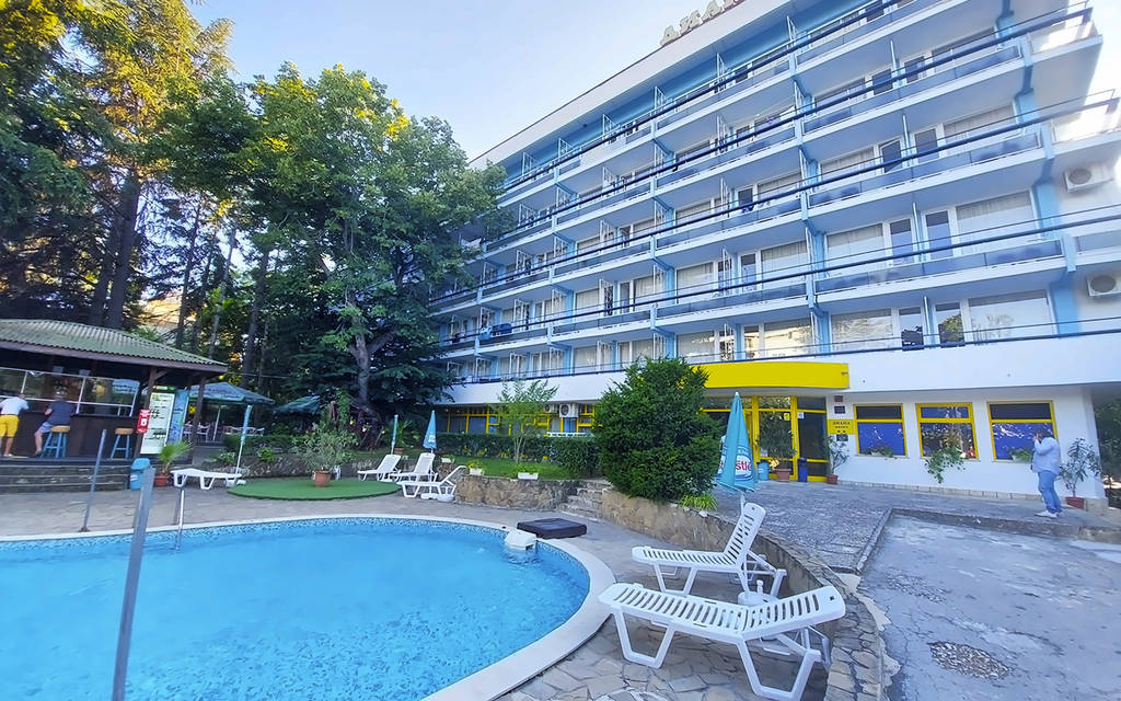 Budova hotelu s bazénem, lehátky a stromy v pozadí. - Budova hotelu s bazénem, lehátky a stromy v pozadí.