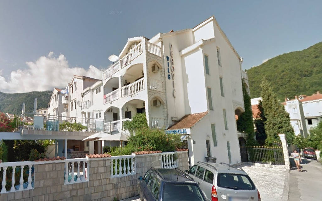 Vnější pohled na bílou hotelovou budovu s balkony a zelenými kopci v pozadí. - Vnější pohled na bílou hotelovou budovu s balkony a zelenými kopci v pozadí.