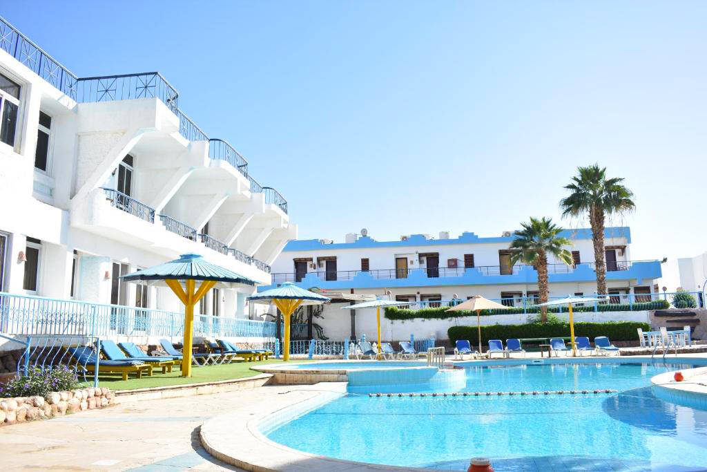 Exteriér hotelu s bazénem, palmami a lehátky pod modrou oblohou. - Exteriér hotelu s bazénem, palmami a lehátky pod modrou oblohou.