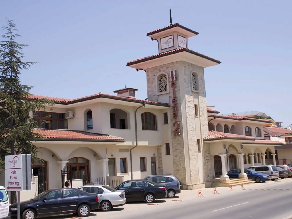 Exteriér hotelu s vysokou hodinovou věží a zaparkovanými auty. - Exteriér hotelu s vysokou hodinovou věží a zaparkovanými auty.