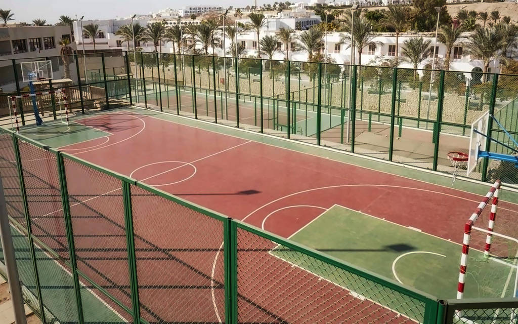 Basketbalové hřiště s červeným a zeleným povrchem, obklopené palmami a jasnou oblohou. - Basketbalové hřiště s červeným a zeleným povrchem, obklopené palmami a jasnou oblohou.