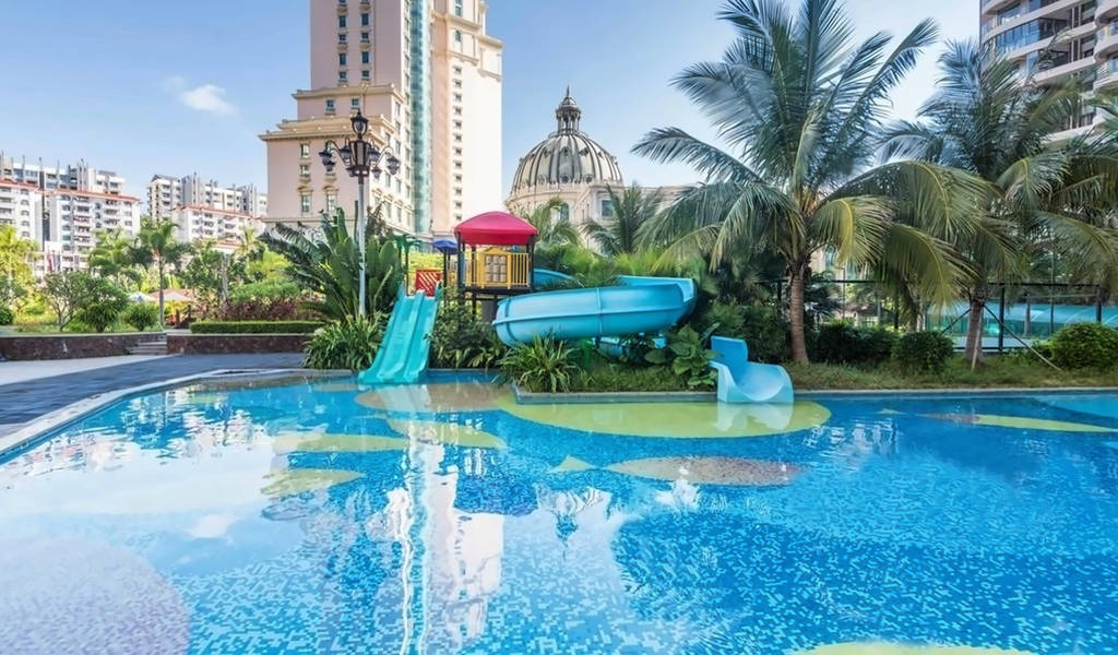 Barevná vodní skluzavka a herní zóna vedle bazénu s palmami. - Barevná vodní skluzavka a herní zóna vedle bazénu s palmami.